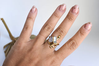 Hand wearing a gold ring with a clear gemstone on a neutral background